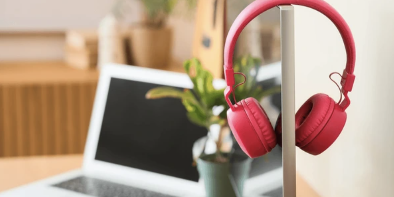 past Event - Red headphones hanging on computer monitor with laptop and plant on wooden desk, home office setup, a laptop and a green potted plant are visible on the wooden desk